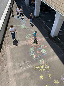 Eine Gruppe von Menschen, die Sozialarbeit leisten, indem sie auf einem Bürgersteig mit Kreidezeichnungen spielen.