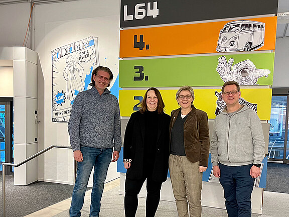 Vier Personen stehen vor einem Schild in einer Lobby  des L64 der AWO in Mönchengladbach.