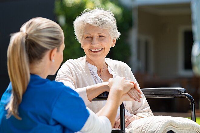 Eine Krankenschwester spricht mit einer älteren Frau im Rollstuhl.