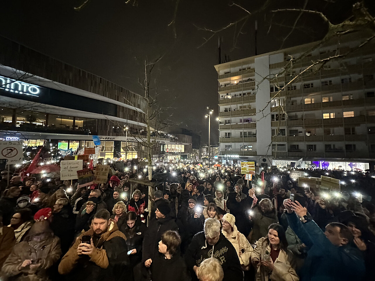 Eine Gruppe Demonstranten stehen friedlich nebeneinander im Dunkeln und halten ihr Smartphone-Taschenlampen hoch.