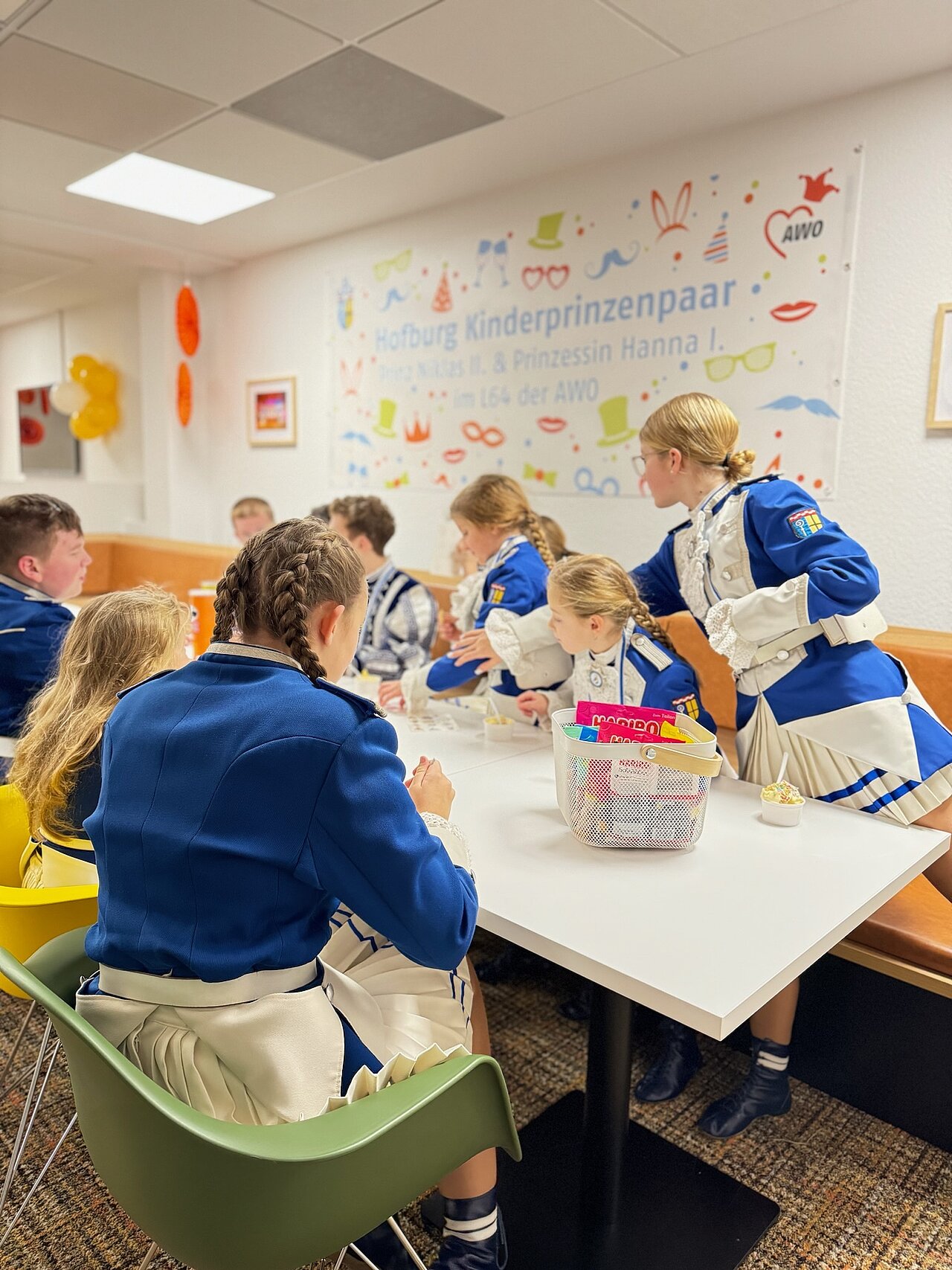 Eine Gruppe Kinder sitzt als Mönchengladbacher Kinderprinzenpaar verkleidet an einem Tisch in einem Büro.